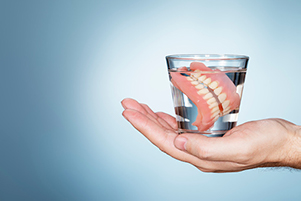 Dentures in a glass of water sitting on the palm of a hand at Uptown Family Dental in Portland, OR